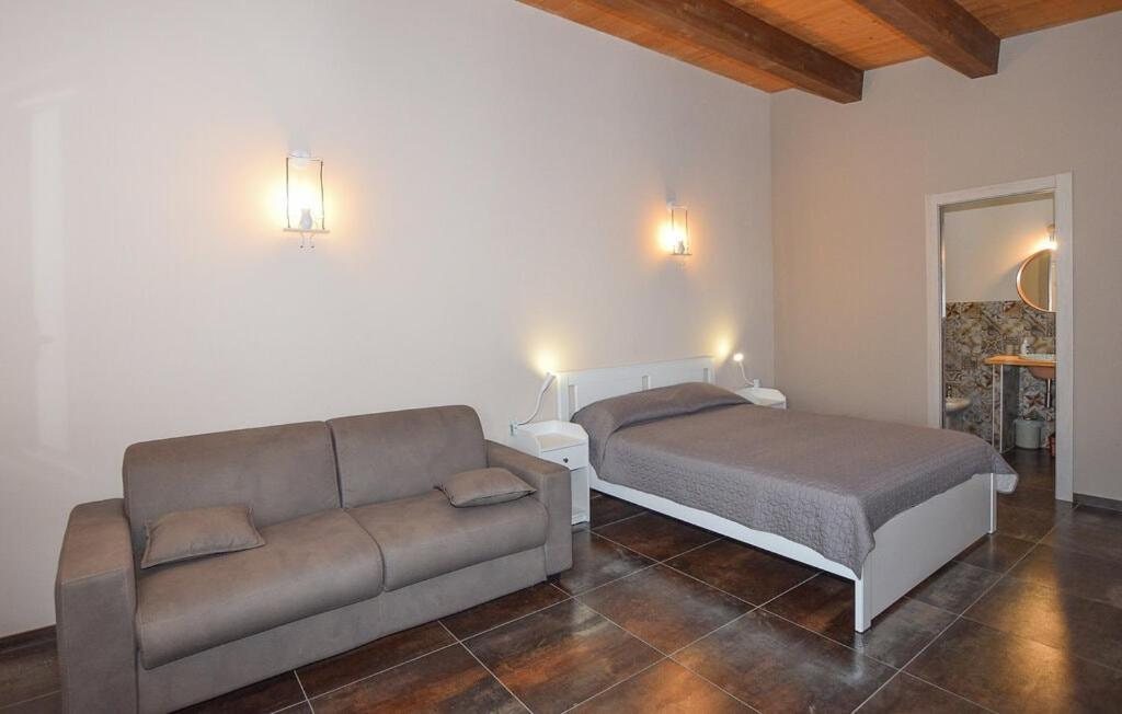 La Camera Quadrupla con il divano letto grigio, il letto matrimoniale e le travi in legno