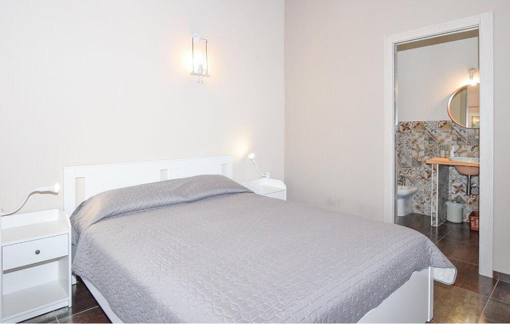 Il letto matrimoniale con il copriletto grigio e la porta del bagno della Camera Quadrupla
