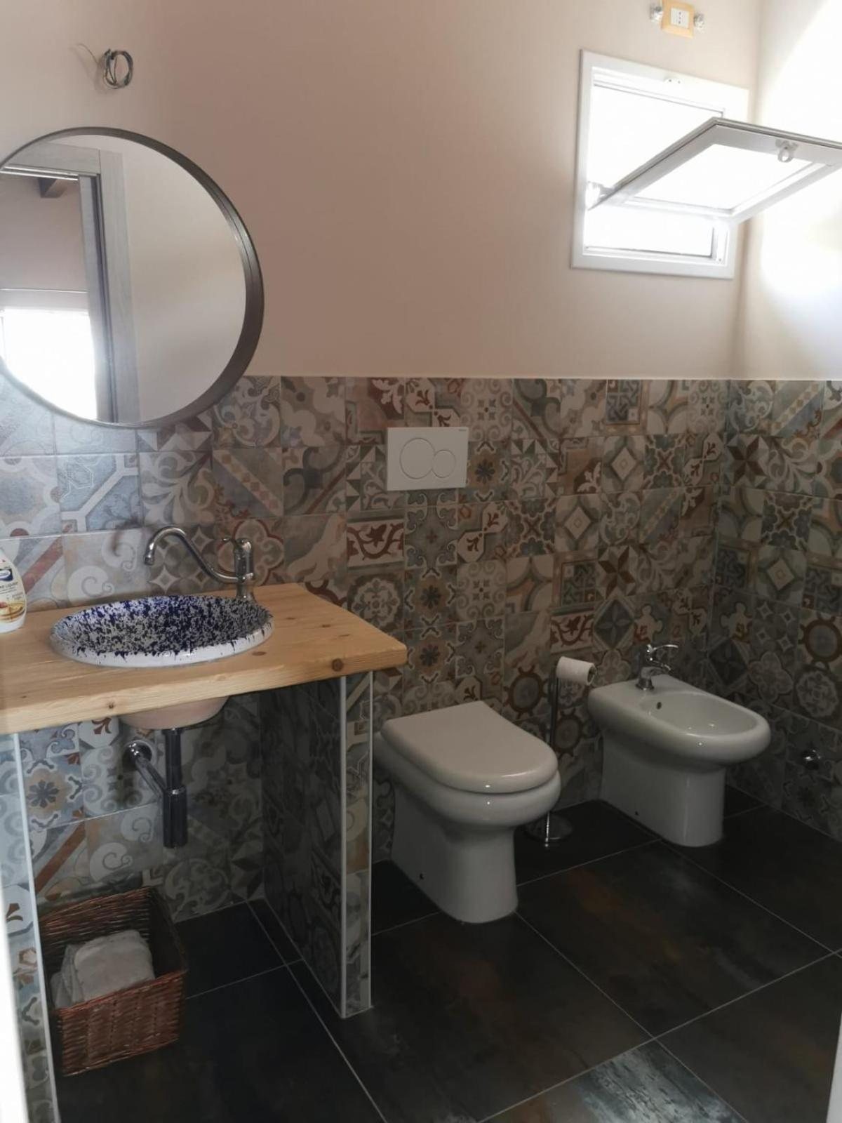 Il lavabo in ceramica decorata e lo specchio tondo nel bagno della Camera Quadrupla