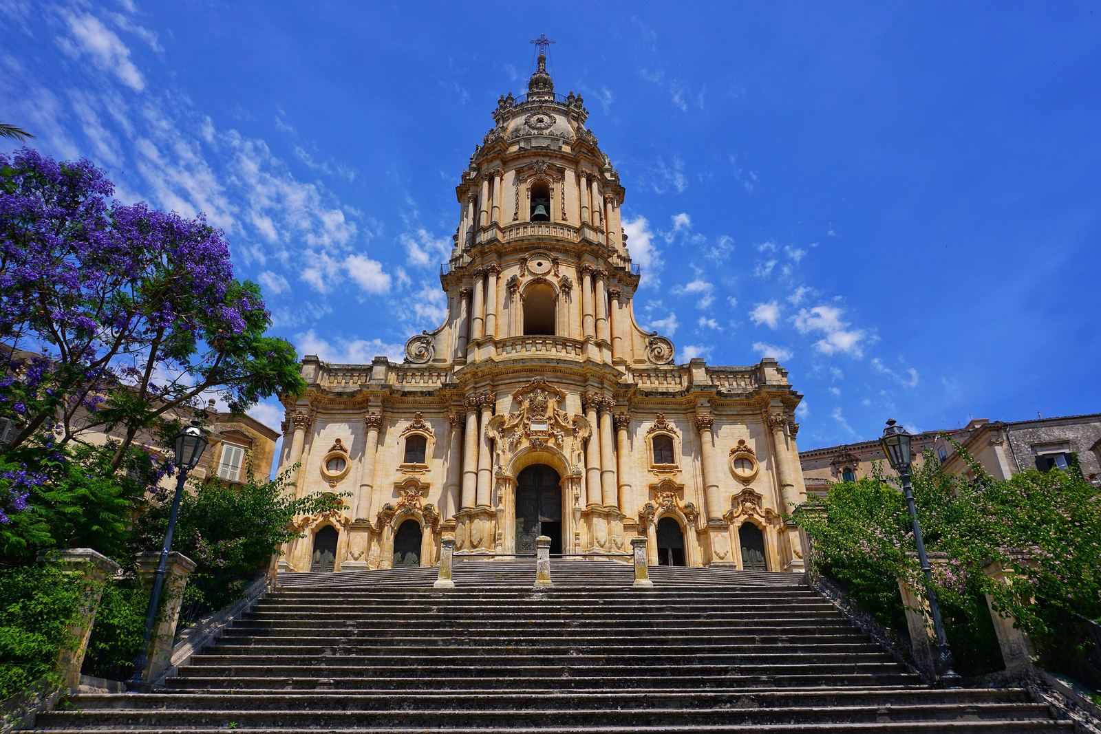 Duomo di San Giorgio a Modica in cima alla scalinata monumentale, tra jacarande in fiore.