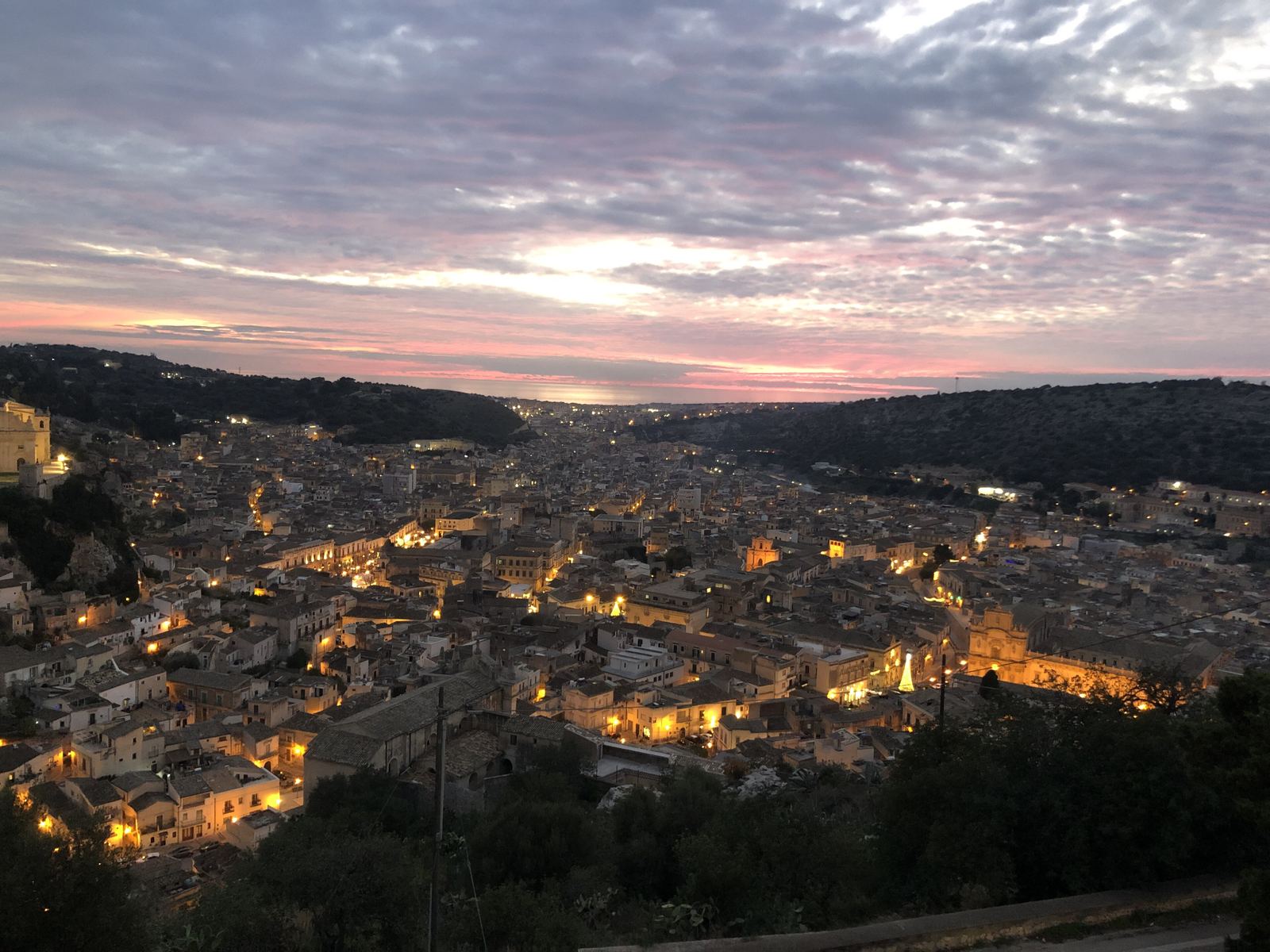 Scicli al tramonto con le luci del centro storico accese nella valle tra le colline.