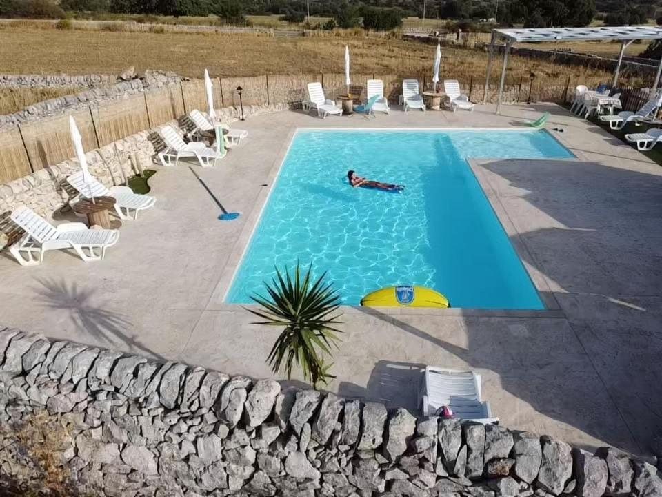 La piscina vista dall'alto, fra il muro a secco, i lettini e la campagna